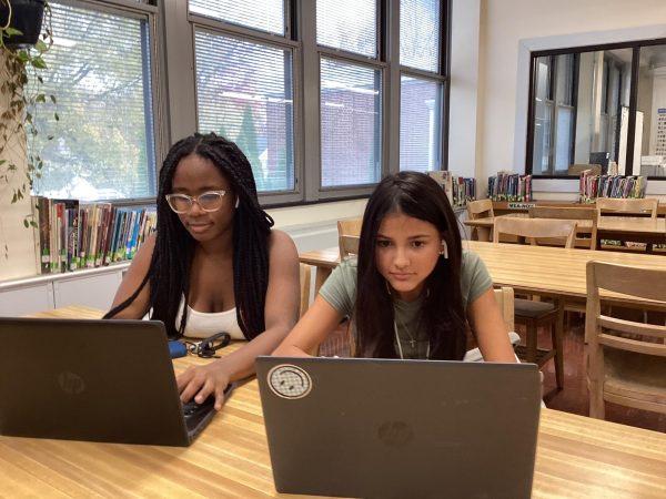 Two students using Airpods to listen to music while they work in the Media Center. 