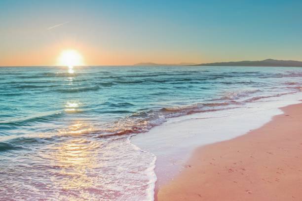 Colorful sunset viewed from the pink sea beach with soft waves.
